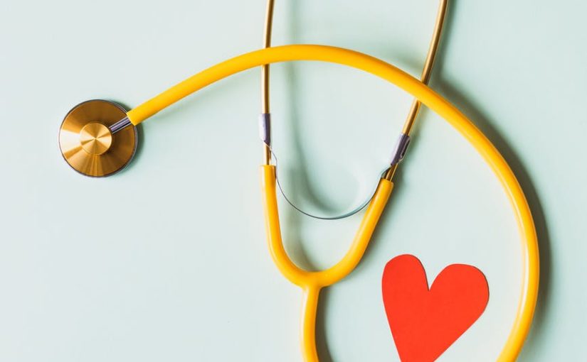 medical stethoscope with red paper heart on white surface